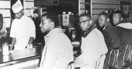 Photograph of four young, Black students sitting at a lunch counter at Woolworth's in Greensboro, North Caroline. They are participating in a sit-in protest to call attention to segregation in the Southern United States.