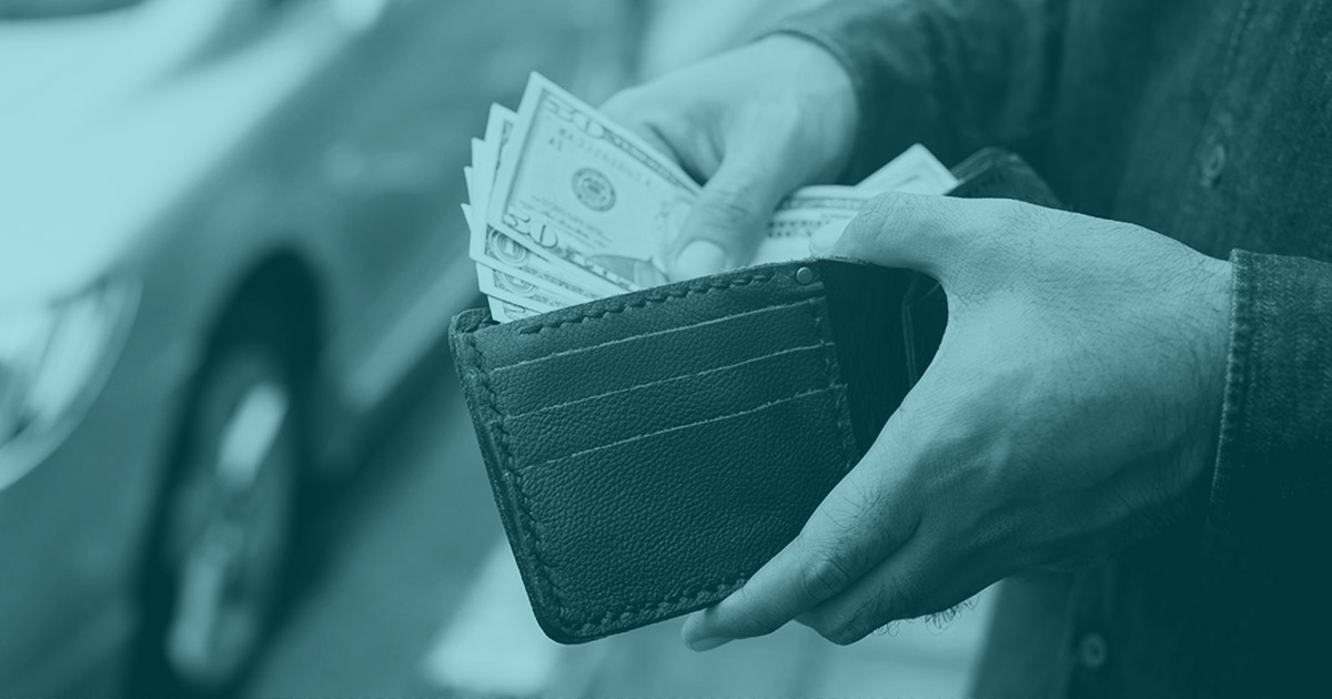 A person holding open a wallet and thumbing through U.S. dollars.