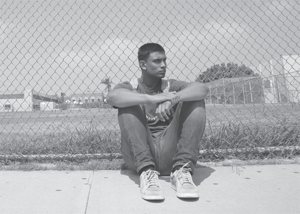 teenager sitting on the ground in front of a chain link fence