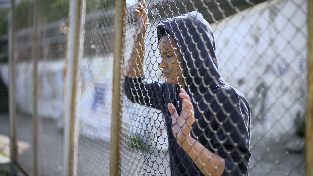 young man of color behind fence enclosure