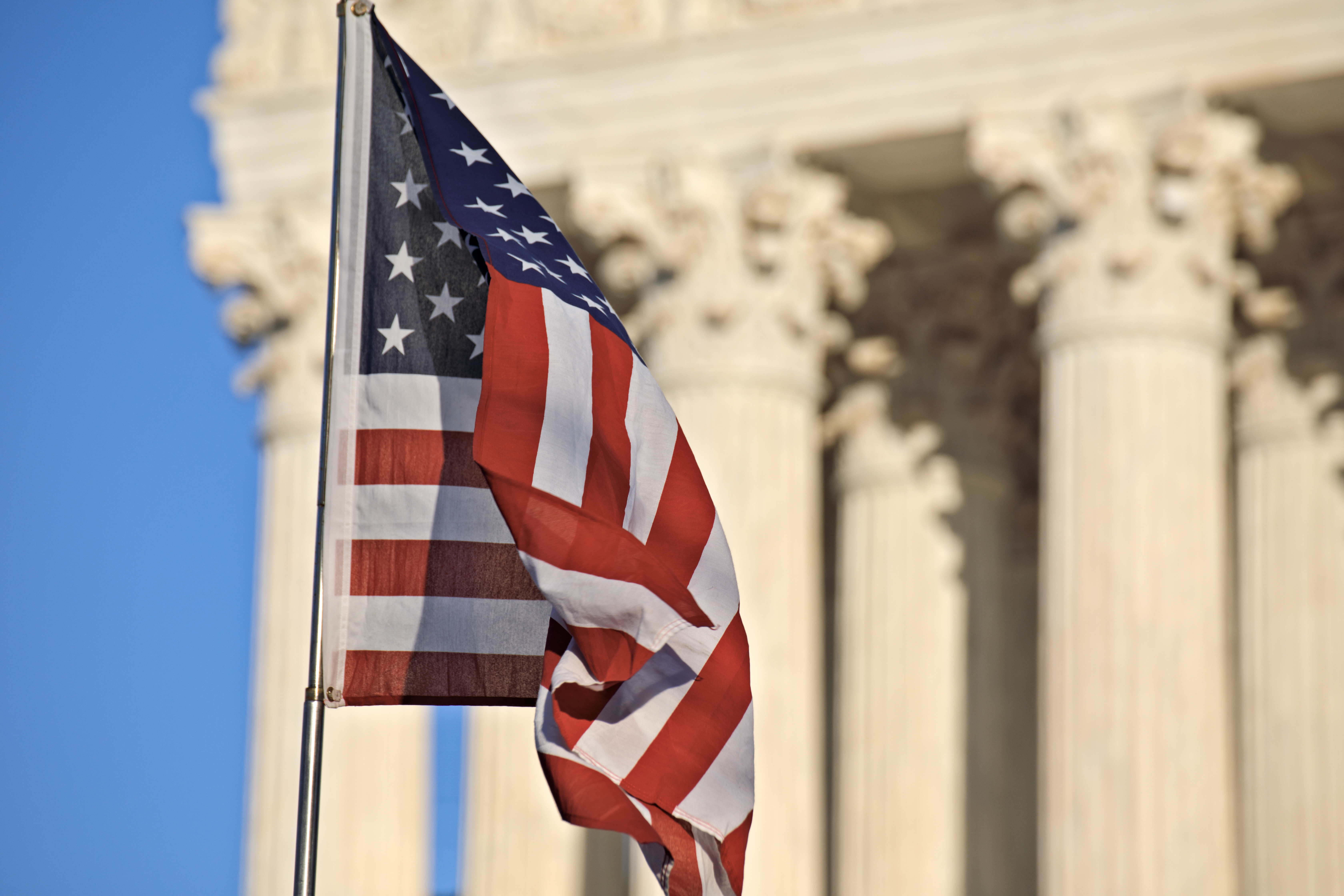 American flag waving in front of the U.S. Supreme Court building columns on Capitol Hill in Washington, DC