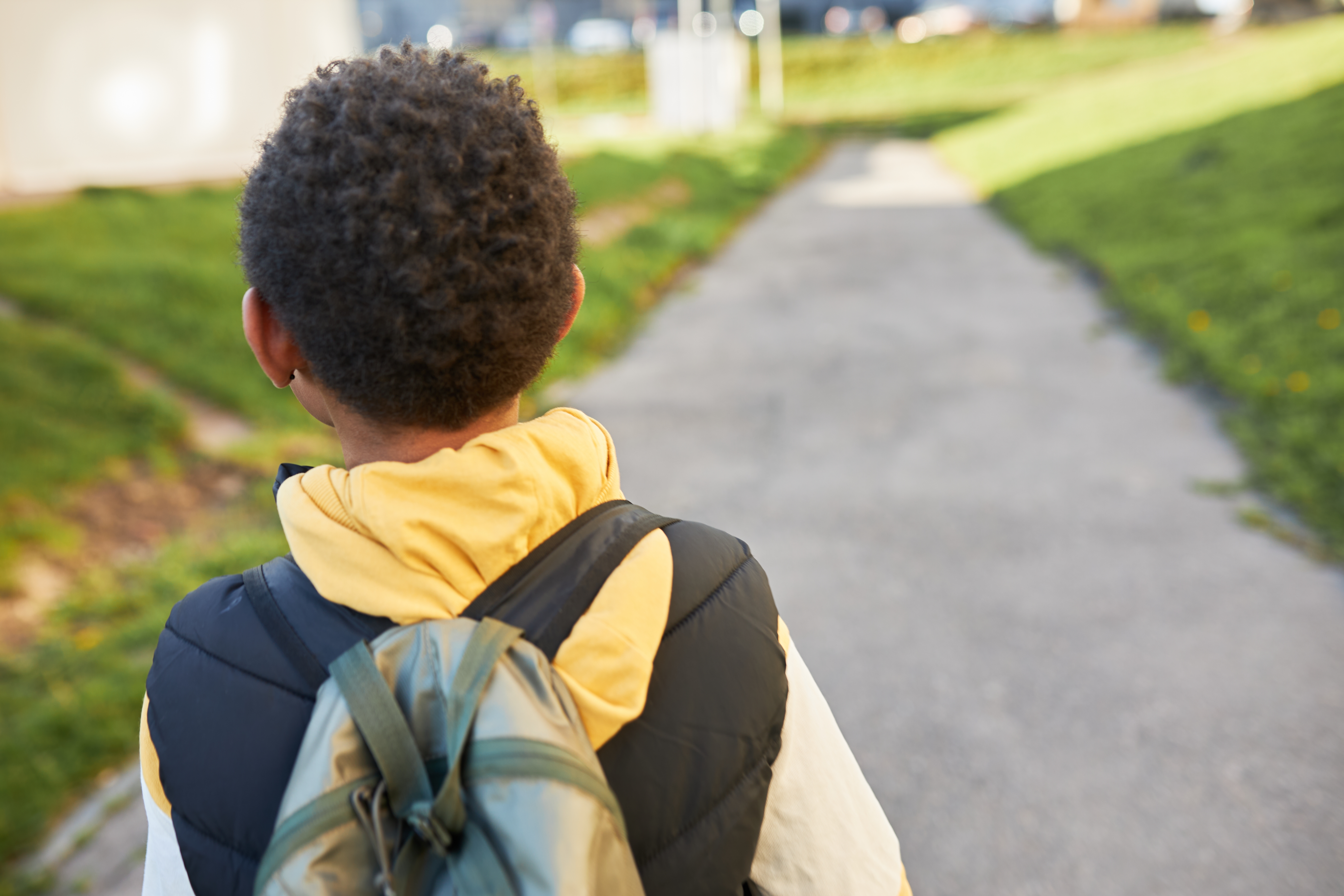 Back view of black child with curly short hair carrying backpack on shoulders