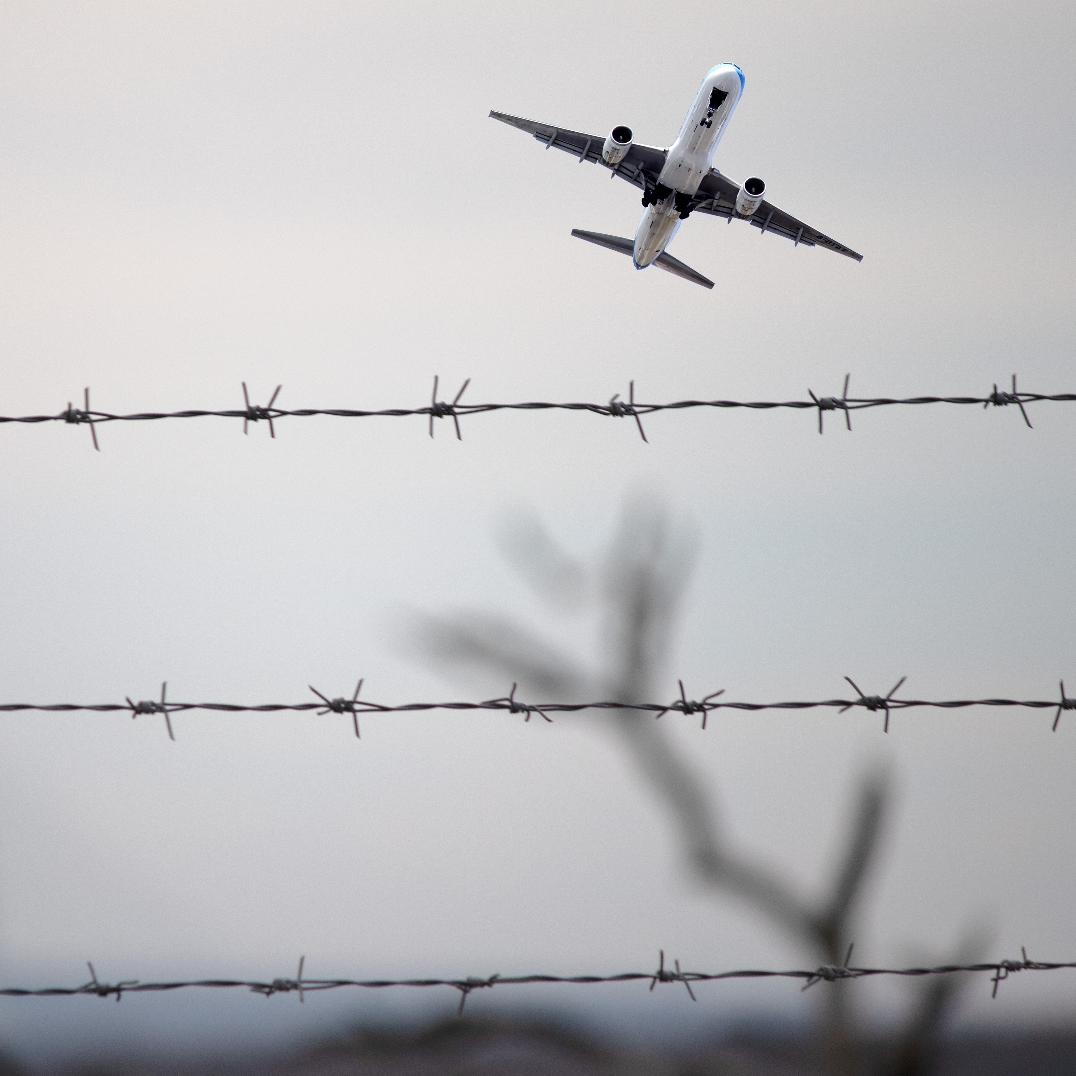 plane flying with barbed wire fence in foreground