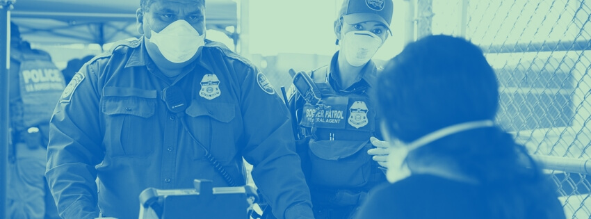 Customs and Border Patrol officer questioning a person at a port of entry. Both are wearing face masks.