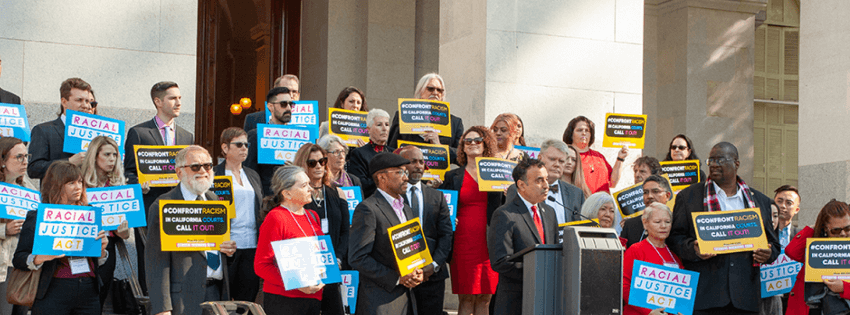 Group of people around a speaker infront of a capital building