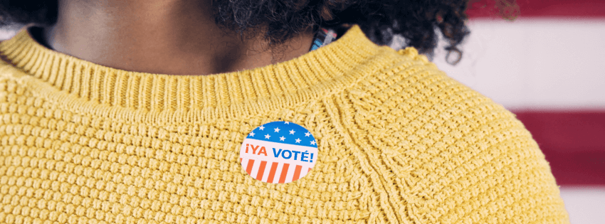 Cropped photograph of a person wearing a yellow sweater with a ¡Ya voté! sticker