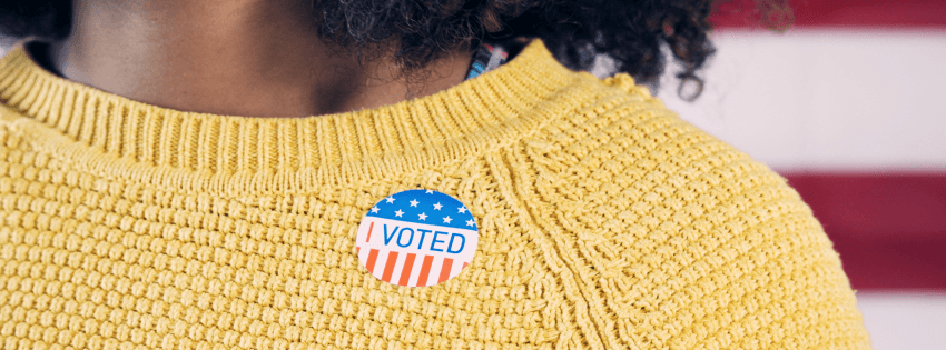 Cropped photo of a woman of color wearing a yellow sweater with an 'I Voted' sticker