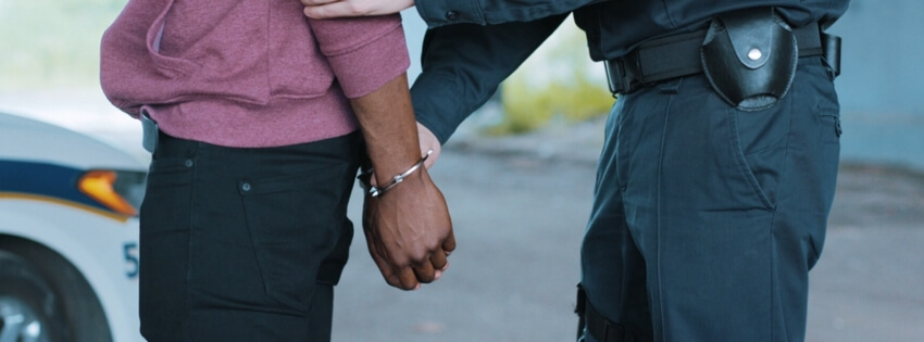 Black man with his hands behind his back and being placed in handcuffs by a uniformed police officer