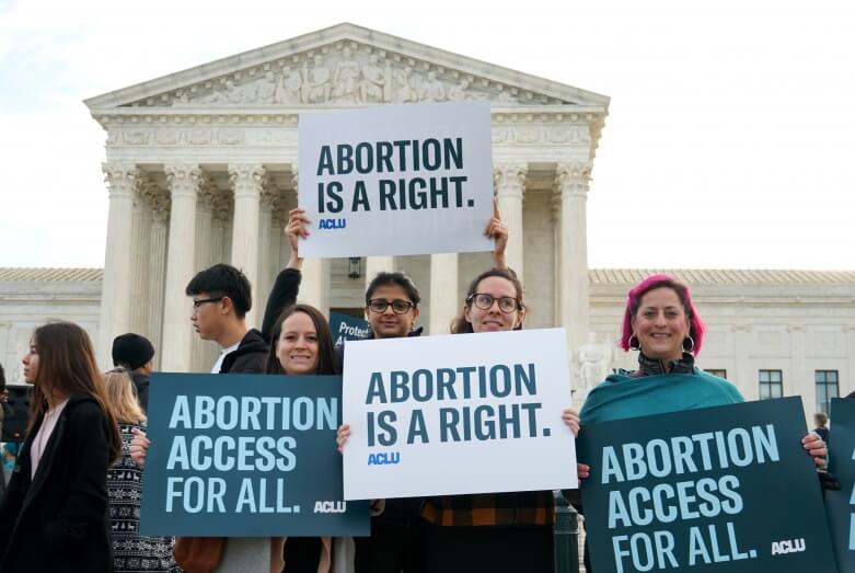 Four people holding signs outside of the Supreme Court that read "Abortion is a right" and "Abortion access for all" 