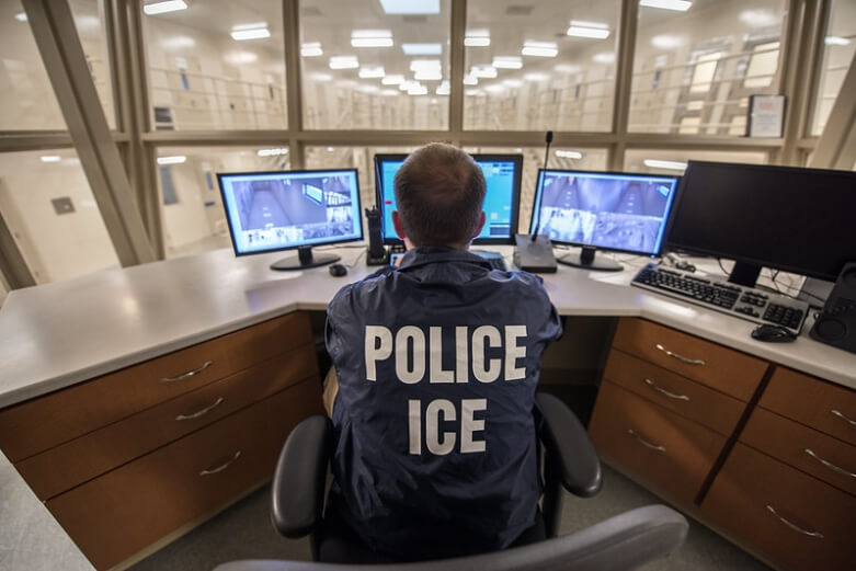 Police officer sitting at desk with three computer monitors 