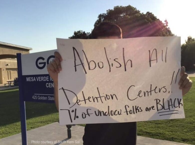 Photo of child outside the Mesa Verde Detention Facility holding a sign that reads, "Abolish all detention centers; 7 percent of undocumented folks are Black"