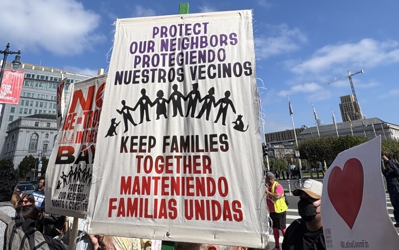 Protest sign reading "Protect our neighbors, keep families together" in English and Spanish