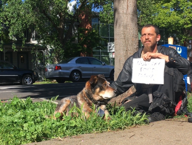 Plaintiff James "Faygo" Clark sits by a Sacramento street corner with a sign and his dog.