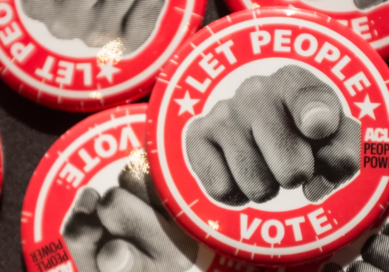 Several buttons on a table, the buttons say LET PEOPLE VOTE and have an image of a hand pointing