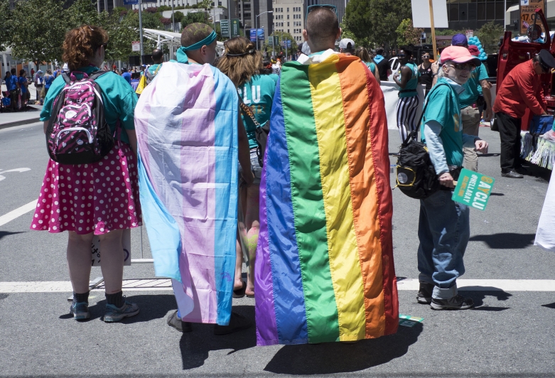 People walking in with Rainbow and Transgender Flags around Necks
