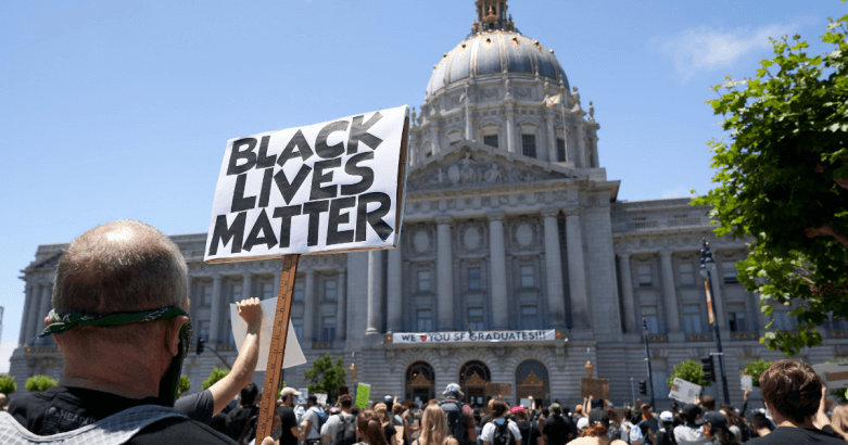 a person is holding a sign that says Black Lives Matter in front of the San Francisco City Hall building