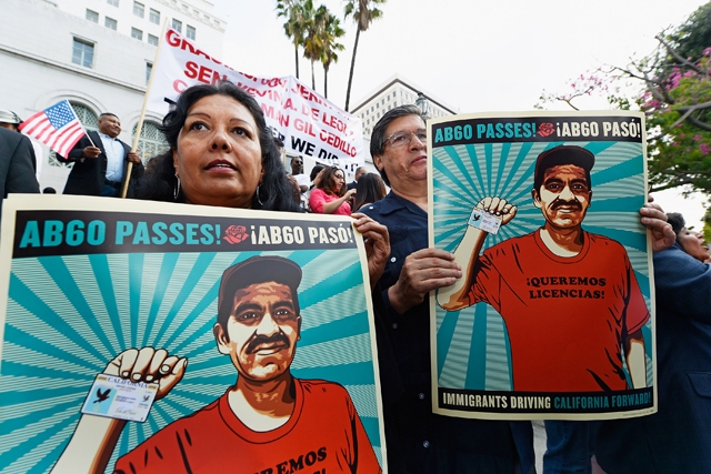 People at a rally for AB 60, holding signs that say "AB60 Passes! Immigrants Driving California Forward"