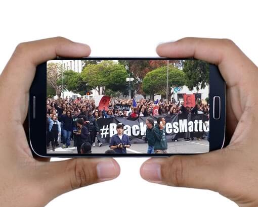 Cell phone in hands with Black Lives Matter protest on screen.