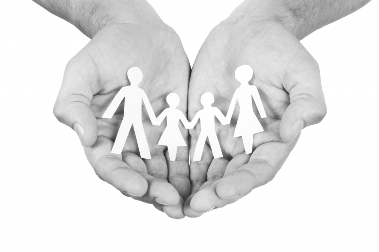 Black and white photo of cupped hands holding a paper cut-out of a family