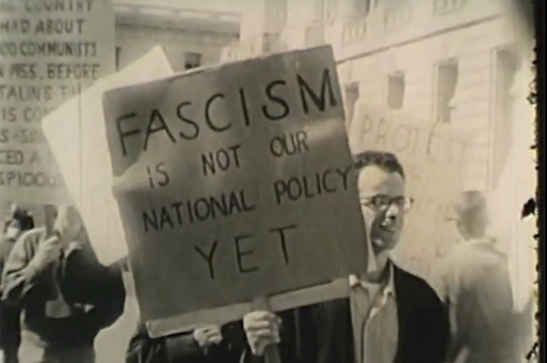 man holds sign saying "Fascism is not our national policy yet"