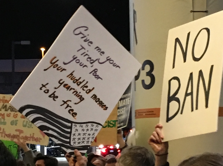 Signs at SFO protest read "No Ban"