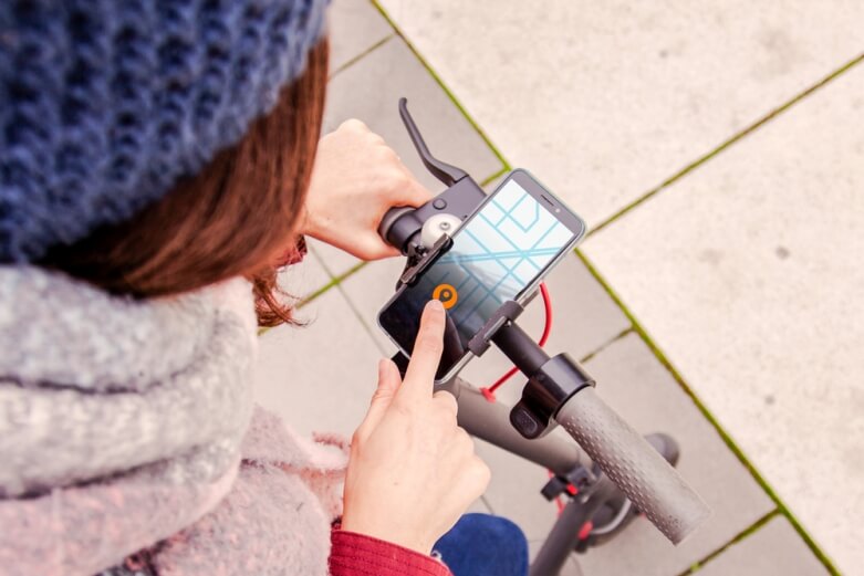 Woman operating mobile application standing atop scooter