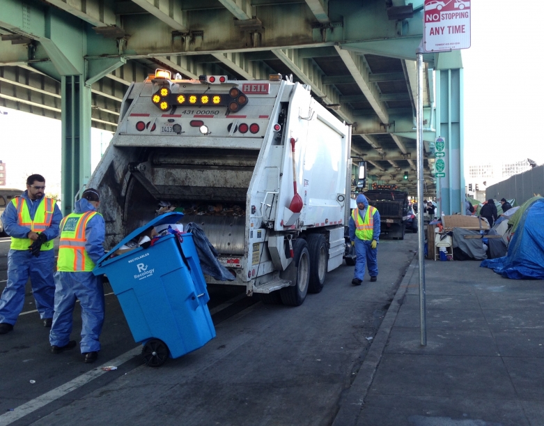 Workers throw homeless people's property into a Caltrans truck