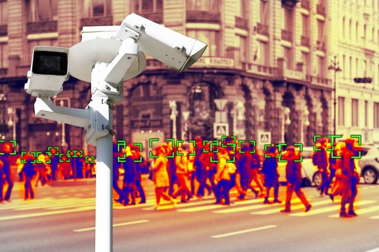 A photograph of surveillance camera in the foreground with a heat map of a gathered crowd in the background.