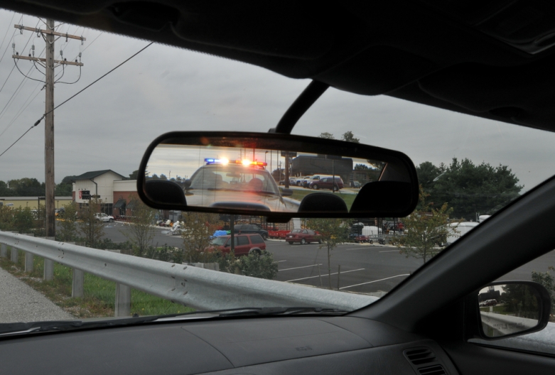 vehicle rear-view mirror showing police cruiser and active lights