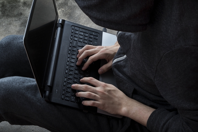 person wearing a hooded sweatshirt typing on laptop