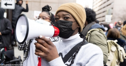 A young Black woman is holding a megaphone at a rally in support of George Floyd