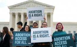Four people holding signs outside of the Supreme Court that read "Abortion is a right" and "Abortion access for all" 
