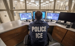 Police officer sitting at desk with three computer monitors 