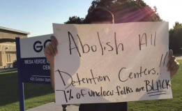 Photo of child outside the Mesa Verde Detention Facility holding a sign that reads, "Abolish all detention centers; 7 percent of undocumented folks are Black" 