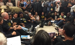 Protestors sit and stand in a circle outside Governor Brown's office