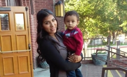 Angelica stands on the steps in front of her school, holding her son Joel
