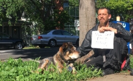 Plaintiff James "Faygo" Clark sits by a Sacramento street corner with a sign and his dog. 