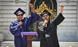 Two young men in caps and gowns raise their fists at a graduation celebration for undocumented immigrants
