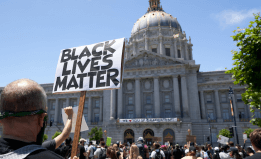 a person is holding a sign that says Black Lives Matter in front of the San Francisco City Hall building