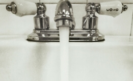Black and white image of water flowing out of a tap into a porcelain sink