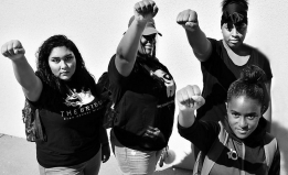 Four female students stand with raised fists, looking up at the camera