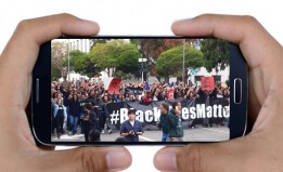 Cell phone in hands with Black Lives Matter protest on screen.