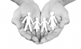 Black and white photo of cupped hands holding a paper cut-out of a family