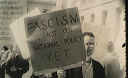 man holds sign saying "Fascism is not our national policy yet"