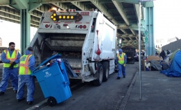 Workers throw homeless people's property into a Caltrans truck