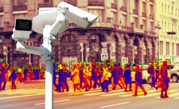 A photograph of surveillance camera in the foreground with a heat map of a gathered crowd in the background.