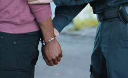 Black man with hands behind his back being placed in handcuffs by a uniformed police officer