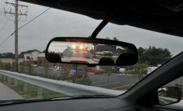 vehicle rear-view mirror showing police cruiser and active lights