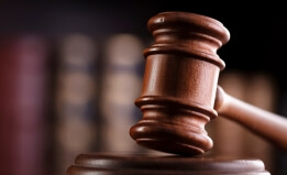 A judge's gavel with law books behind on a shelf behind it. 