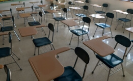 Desks in empty dark high, middle, or elementary school classroom with light coming through windows.
